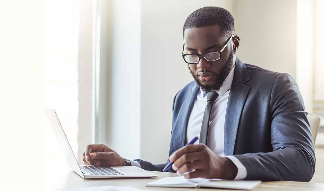 Man working on laptop with pen and paper